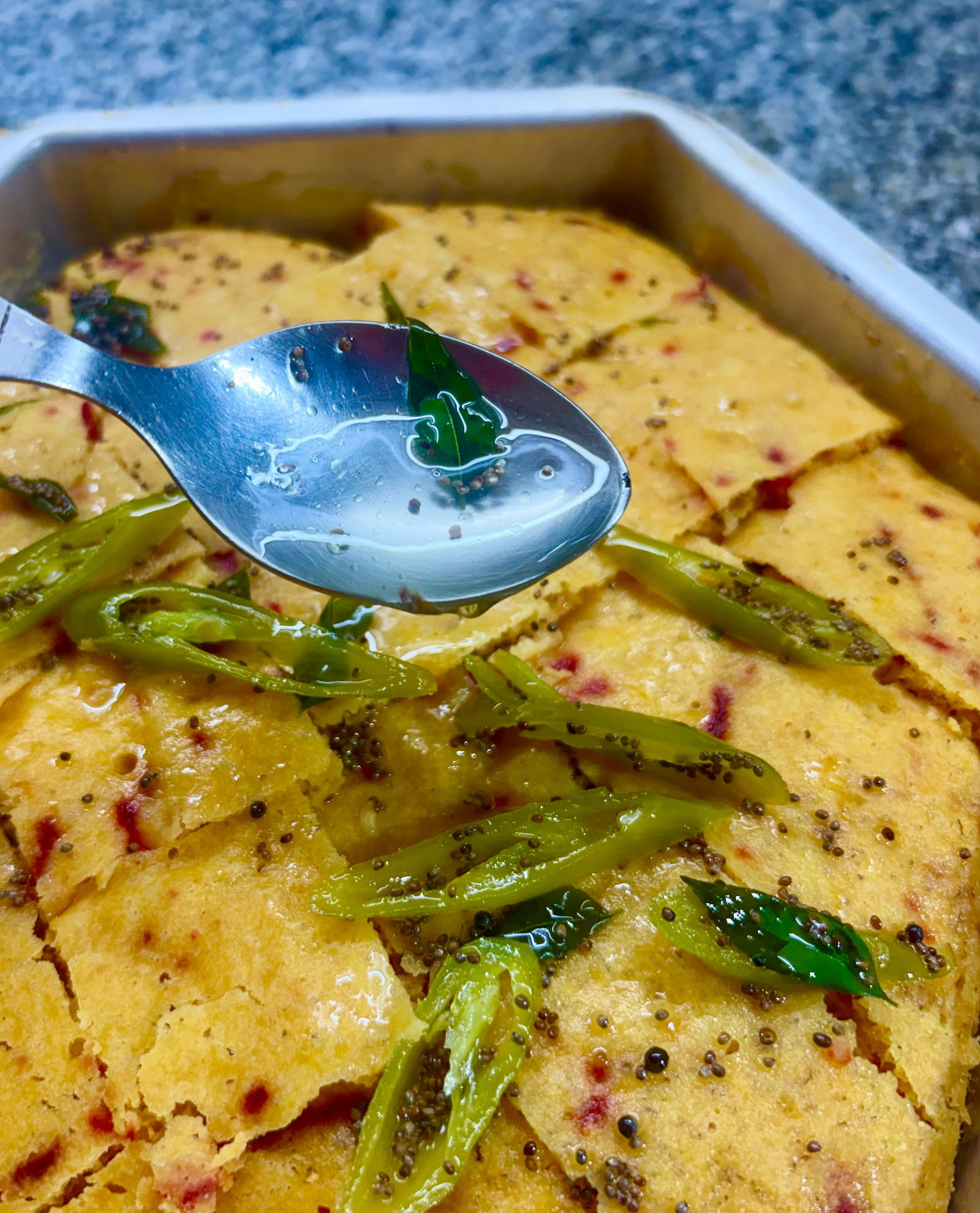Step 5.1: Pour the warm tempering evenly over the sliced khaman, ensuring it seeps into the cuts to keep the dhokla moist