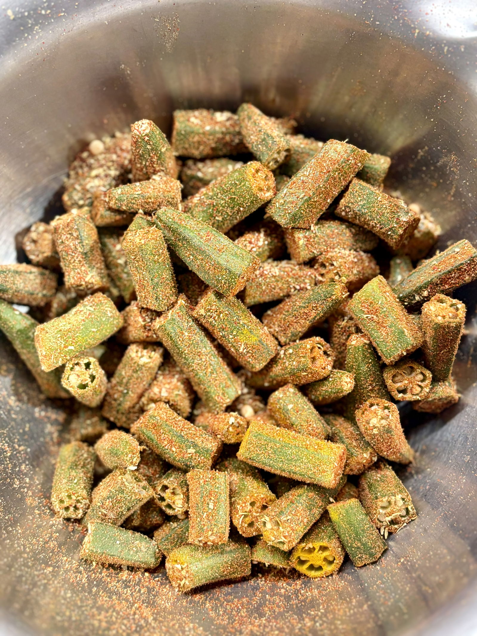 Step 2.1: In a large mixing bowl, toss the cut bhindi (okra) with red chilli powder, turmeric, coriander powder, and amchur powder