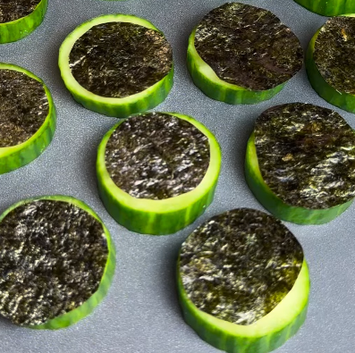 Step 1.1: Place a cucumber ring on each serving tray, top with a hot honey salmon bite, drizzle a small amount of the hot honey glaze over each piece of salmon, and garnish with sesame seeds and cilantro