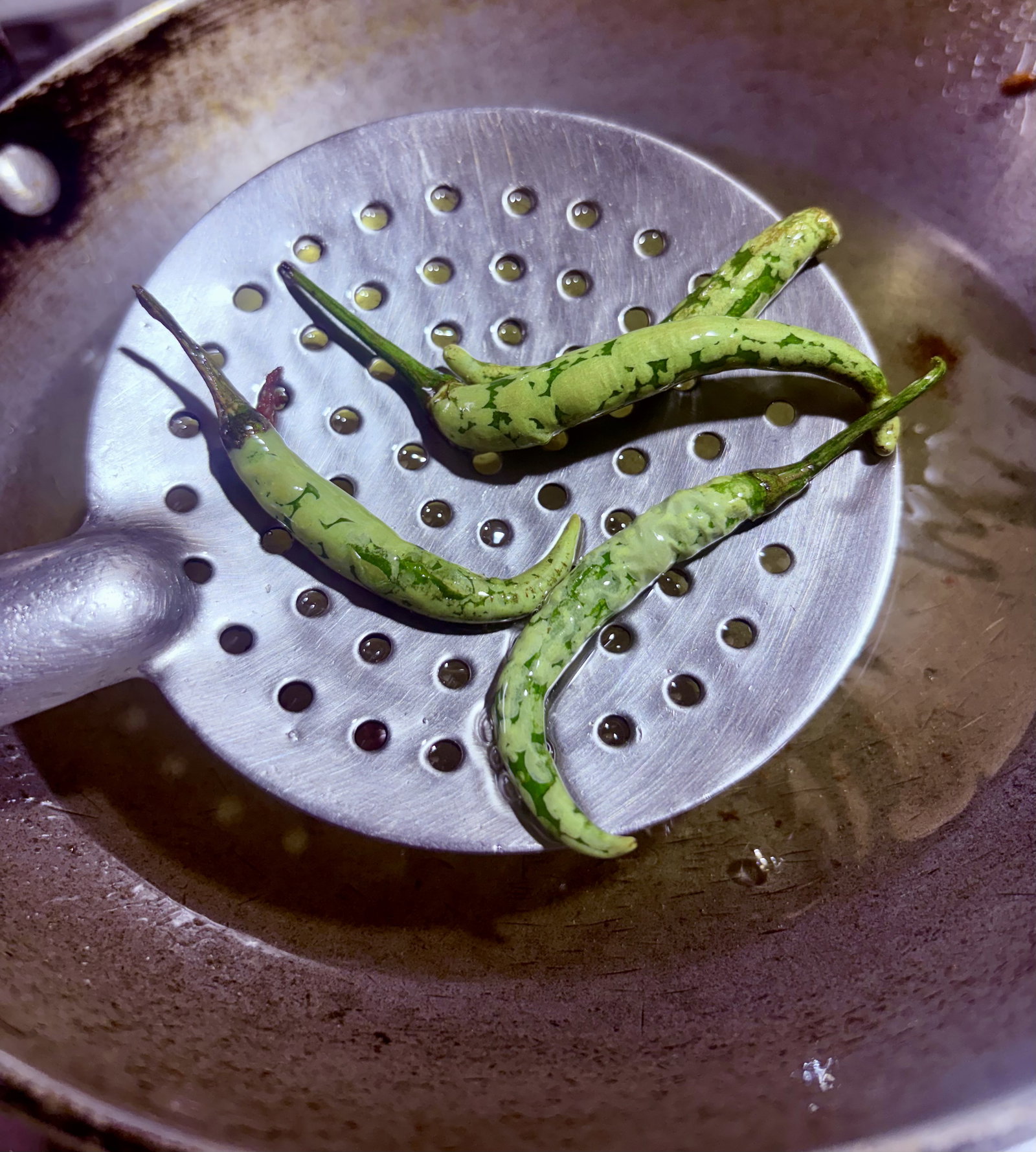 Step 3.1: Add whole green chillies to the same oil and fry for a minute until blistered