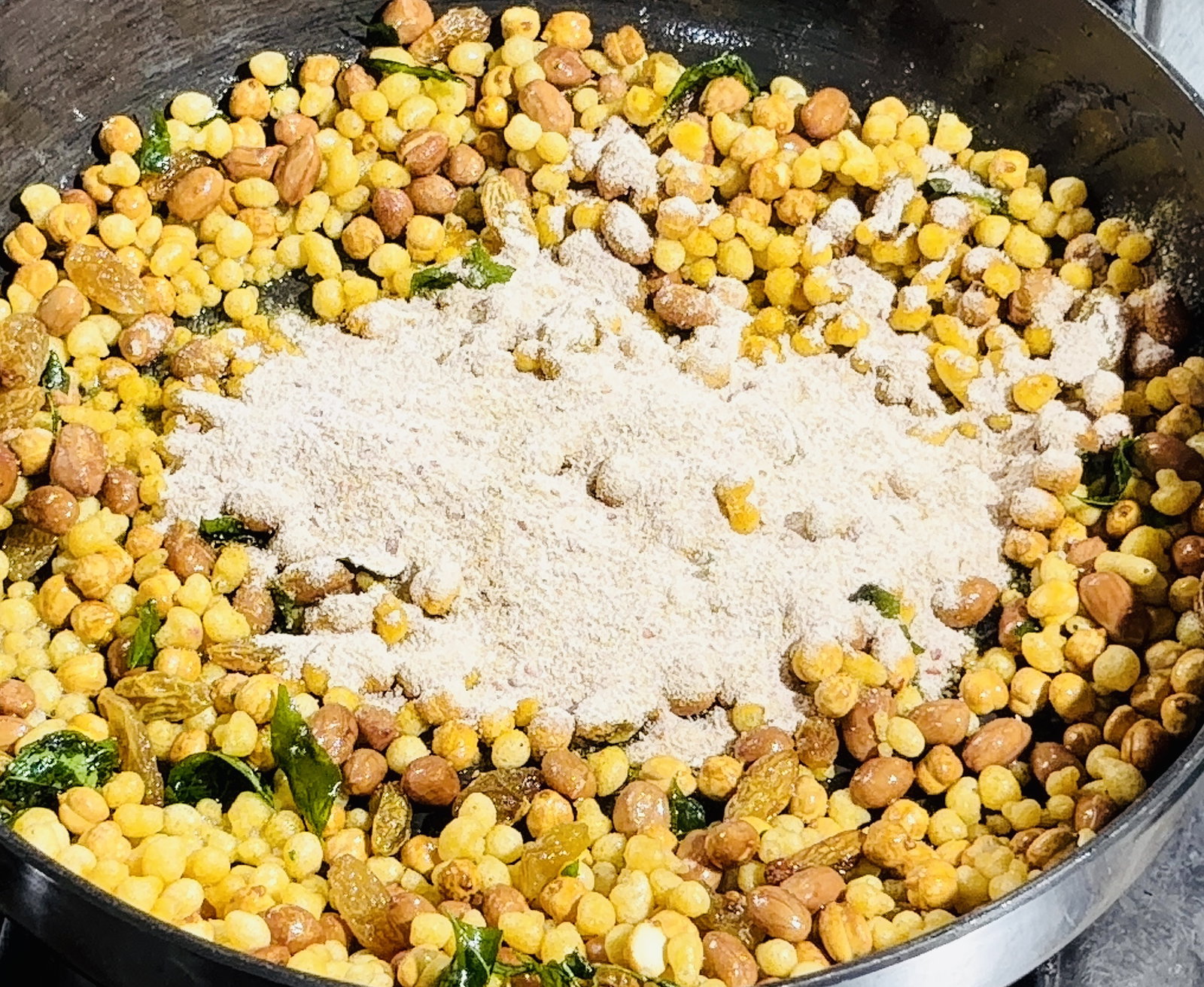 Step 3.1: Sprinkle the prepared spice mix over the mixture and stir quickly to coat the fried nuts, raisins, and boondi evenly