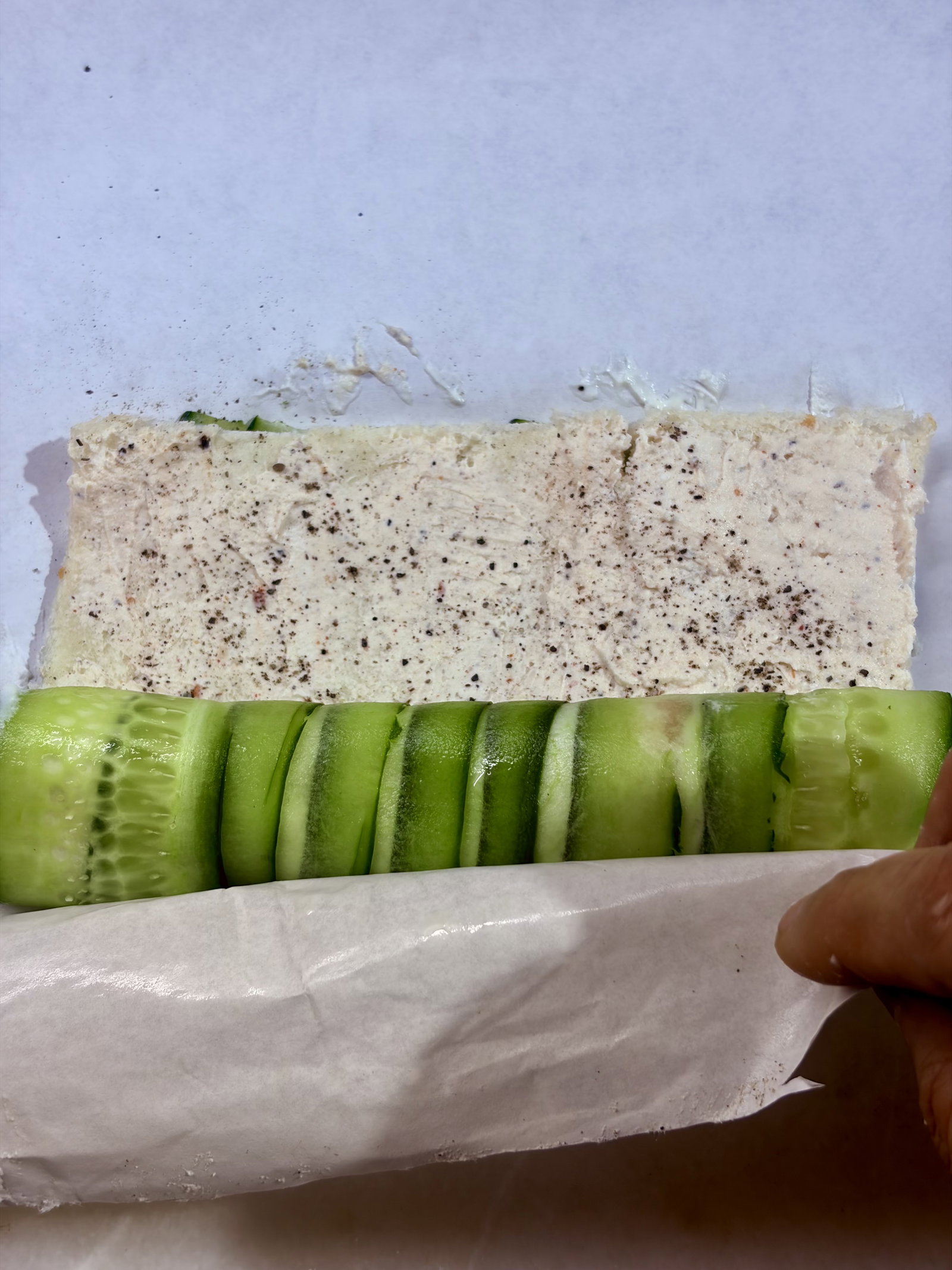Step 5.1: Lift the edge of the parchment paper to start rolling the cucumber mat into a tight log